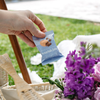 Close-up of Sneaky Wholefoods Peanut Butter Cookie Nourish Bite being taken from a picnic basket, highlighting its gluten-free, plant-based ingredients and convenient packaging