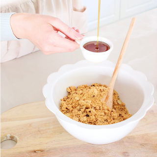 Syrup being poured into Sneaky Wholefoods Peaches and Cream Protein Ball Mix, highlighting how easy it is to prepare these protein-packed, plant-based snacks