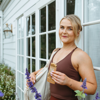 Woman enjoying Sneaky Wholefoods Peanut Butter Caramel Snick Snack Protein Bar after a workout, highlighting its role as a plant-based, high-protein, gluten-free recovery snack.