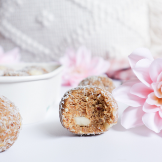 A bitten white chocolate macadamia protein ball, surrounded by a fun, inviting presentation.